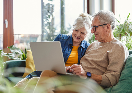A senior couple is sitting on their couch looking at a laptop together